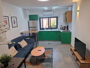 A compact living space with a sofa, a small table, a TV, a kitchen area with green cabinets, and a window.