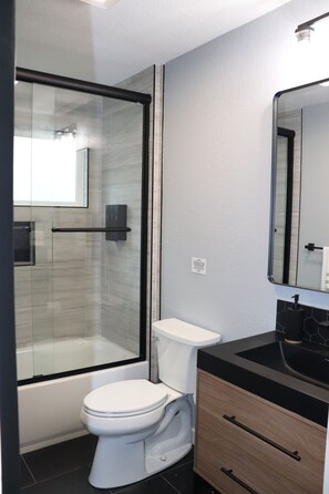 Un baño moderno con cabina de ducha de vidrio, un inodoro blanco y una encimera negra con un espejo arriba.