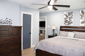 Un dormitorio con cama, cómoda, ventilador de techo y obras de arte en la pared.