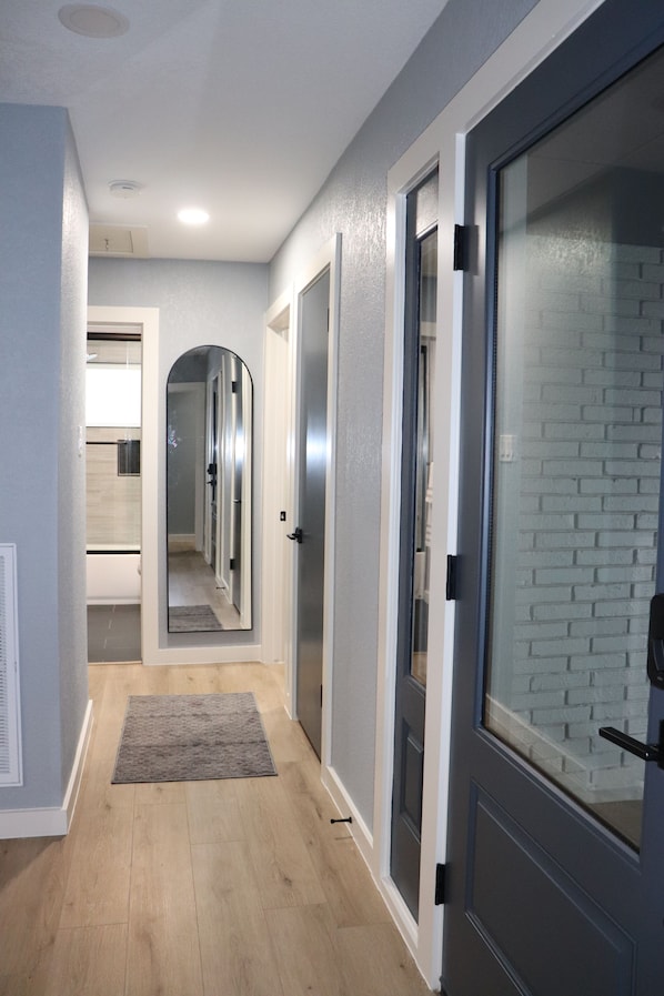 A hallway with a wooden floor, a gray rug, and a door with frosted glass panels.