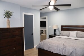 A bedroom with a bed, dresser, ceiling fan, and a door leading to another room.