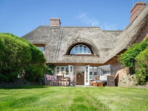 A thatched-roof house with a large arched window, a brick chimney, and a well-maintained lawn. - Holiday Home Dorfhus Anja (Kampen)
