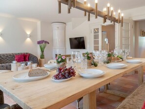 A dining area with a long wooden table set for a meal, a sofa, and a television in the background. - Holiday Home Dorfhus Anja (Kampen)