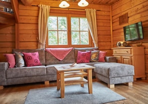 A cozy log cabin interior with a sofa, ottoman, and a television.