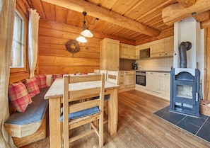 A wooden cabin interior with a dining area, kitchen, and a wood stove.