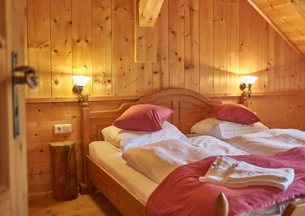 A wooden cabin room with two beds, each with a headboard and bedside lamps.