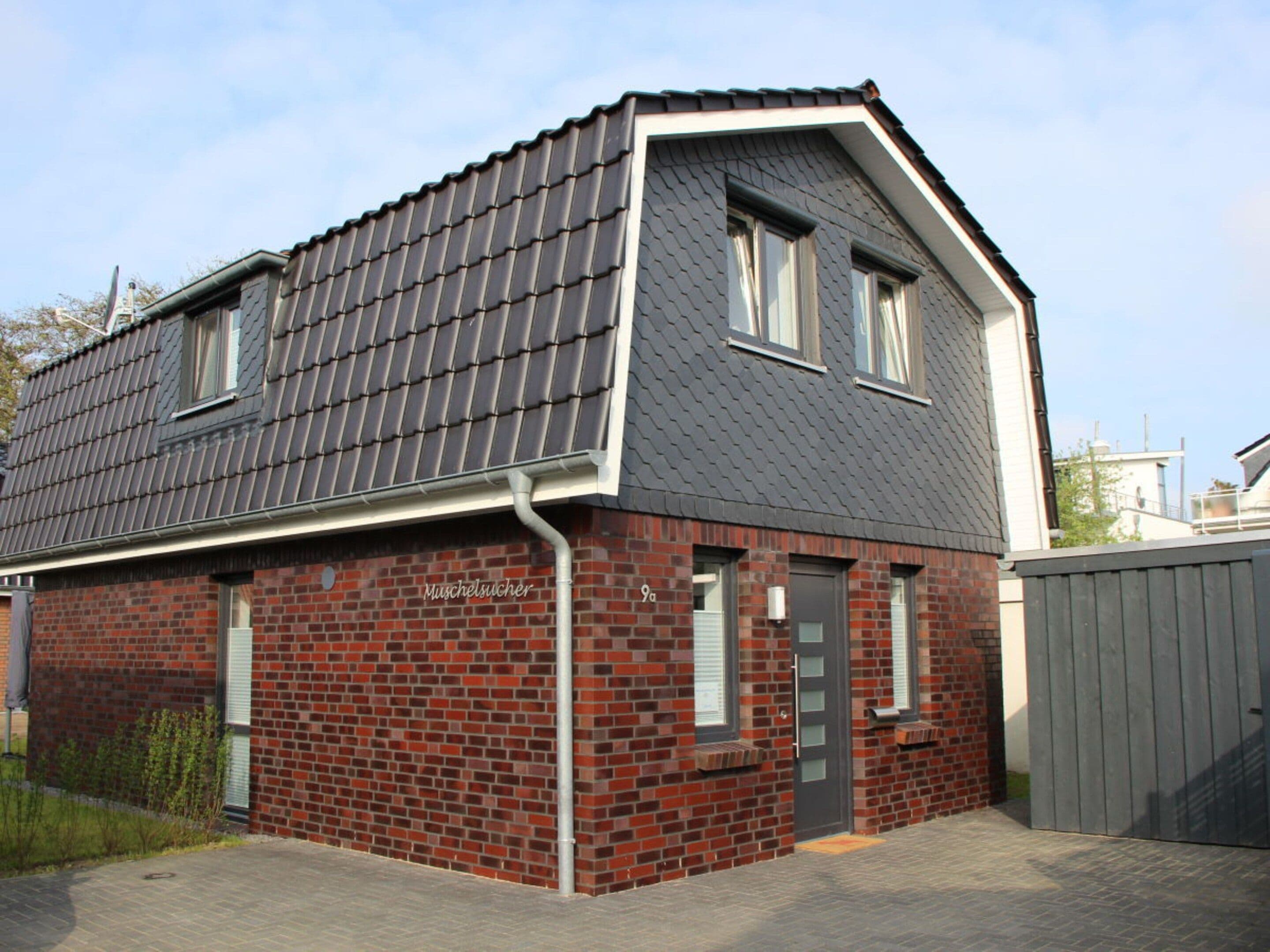 A two-story house with a dark roof, red brick walls, and a grey door.