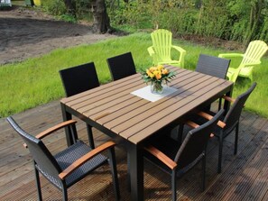 Une terrasse en bois avec une table et des chaises, entourée de verdure.