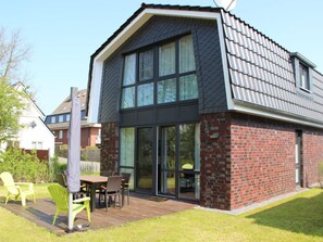 A modern house with a sloped roof, large windows, and a deck with outdoor furniture. - Holiday Home in Cuxhaven With Wi-fi (Cuxhaven)
