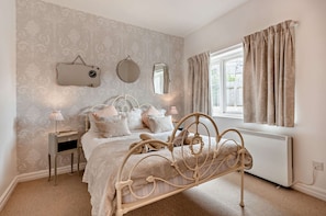 A bedroom with a bed, bedside tables, a mirror, a window with curtains, and a radiator. - Host & Stay - Lindens (Croyde)
