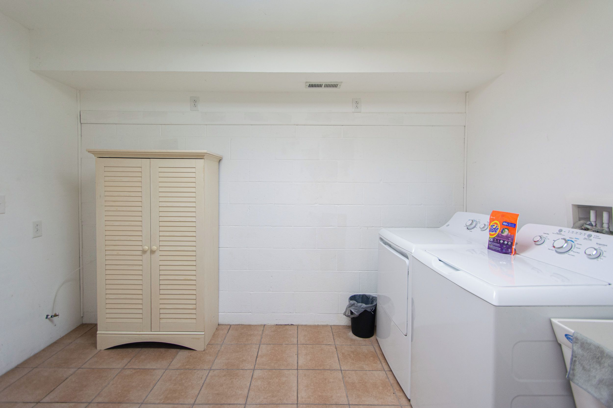 Une buanderie équipée d’un lave-linge, d’un sèche-linge, d’une armoire beige et d’une poubelle.