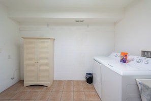 Un lavadero con lavadora, secadora, un armario color beige y un cubo de basura.