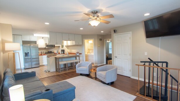 A modern living room with a sofa, ottoman, and a coffee table. There is a kitchen area with cabinets and appliances in the background. - EZ Carriage House by Lake Monroe (Bloomington)