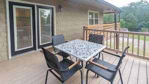 A covered outdoor patio with a table and chairs, a wooden deck, and a view of the surrounding area. - EZ Carriage House by Lake Monroe (Bloomington)