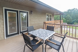 Un patio techado al aire libre con mesa y sillas, una terraza de madera y vistas del entorno.