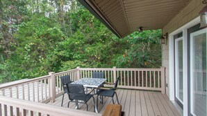 A covered outdoor deck with a table and chairs, surrounded by a wooden railing, and overlooking a lush green landscape. - EZ Carriage House by Lake Monroe (Bloomington)