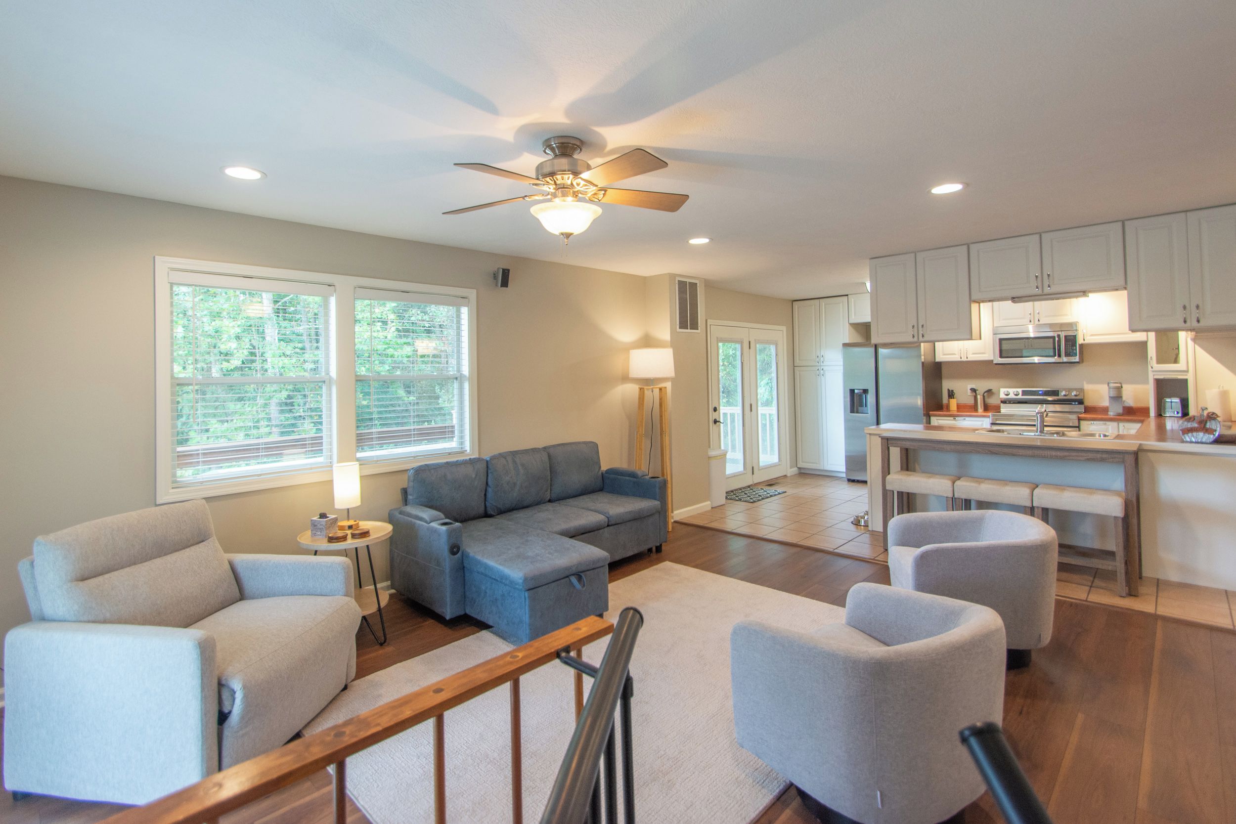 A spacious living area with a gray sofa, two armchairs, a wooden coffee table, and a ceiling fan.