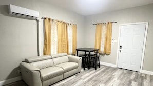 A living room with a sofa, a dining table with chairs, a white door, and an air conditioning unit. - 2BR APT close to Ybor, Downtown, Airport, Busch Gardens & Adventure Island (Tampa)