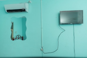 A room with a teal wall, a bed with a red headboard, a white air conditioner, and a television.