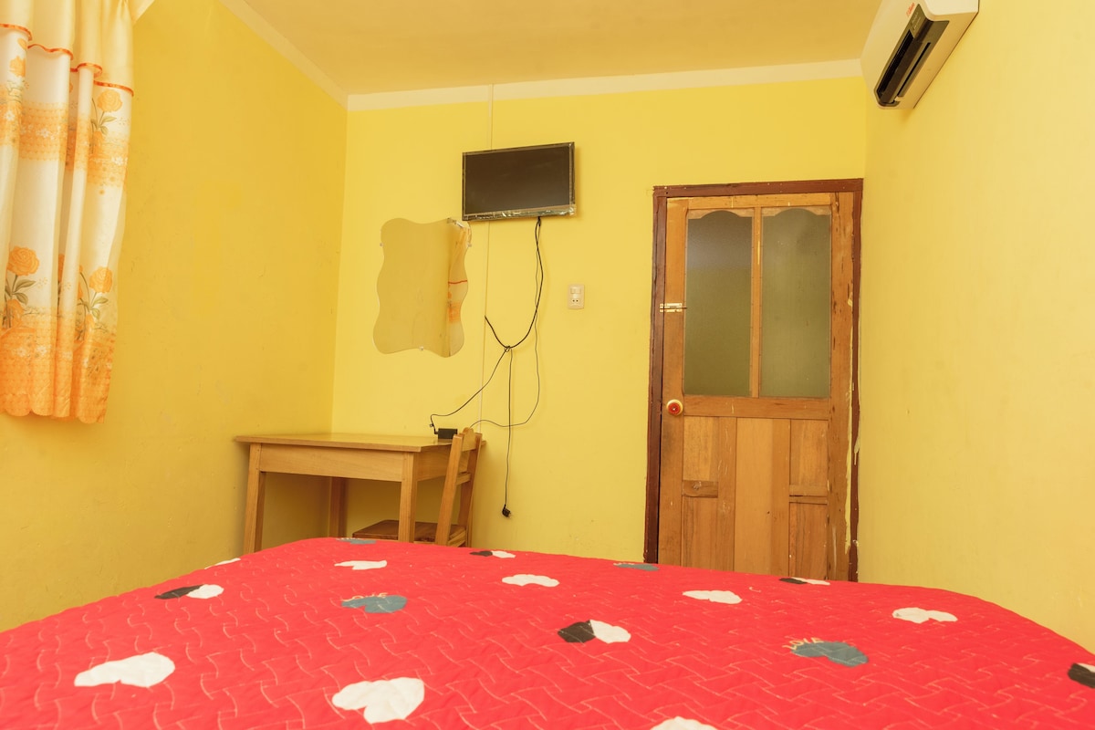 Een kamer met een bed, een bureau, een deur en een tv aan de muur.
