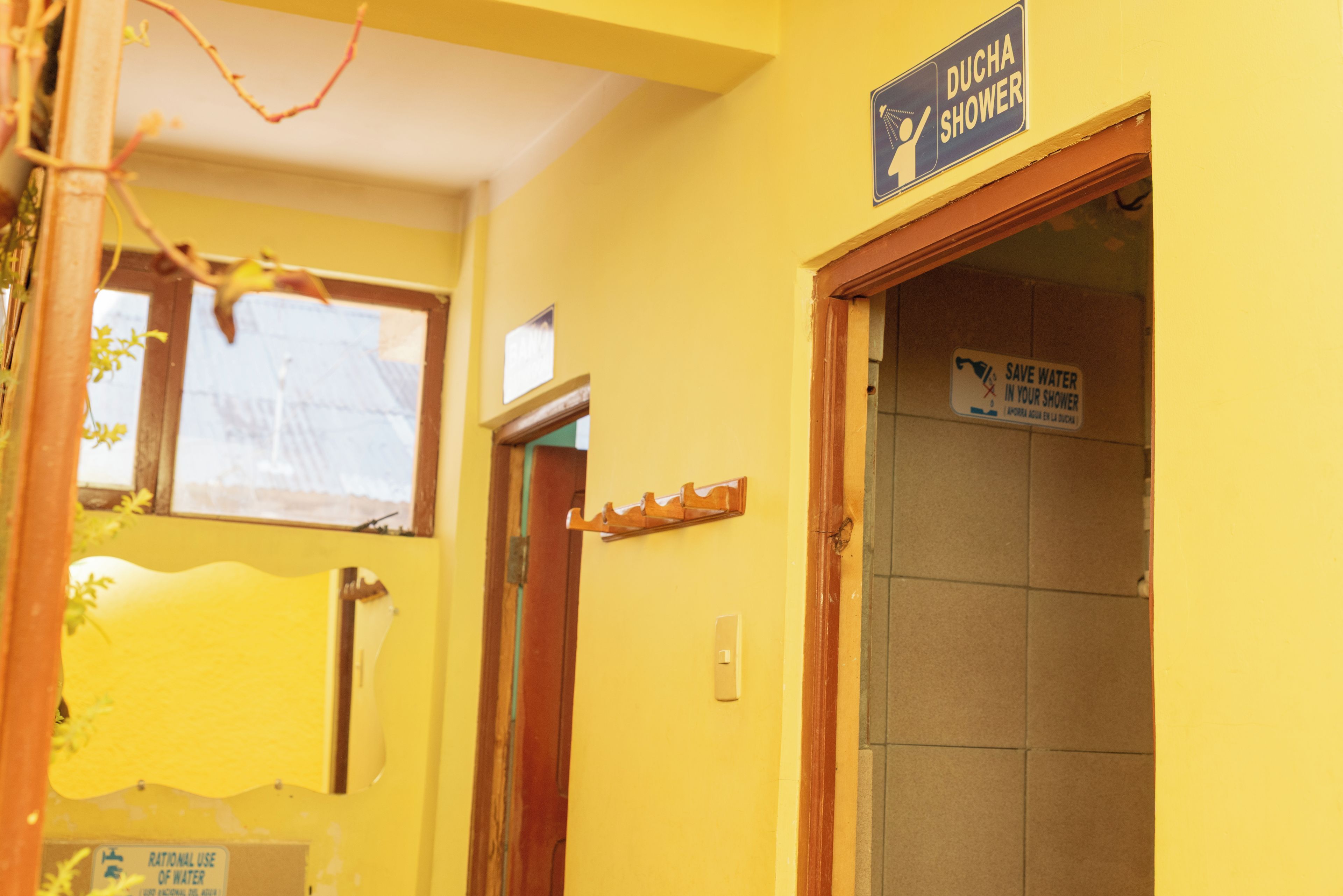 Casa de banho com chuveiro, um sinal a indicar 'DUCHA SHOWER' e um aviso a solicitar 'ECONOMIZE ÁGUA NO SEU CHUVEIRO'.