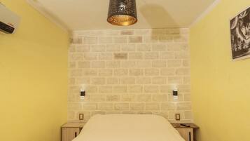 Une pièce avec un mur dont le motif imite un mur de briques, un lit recouvert d’une courtepointe blanche, un luminaire suspendu et une prise de courant fixée au mur.