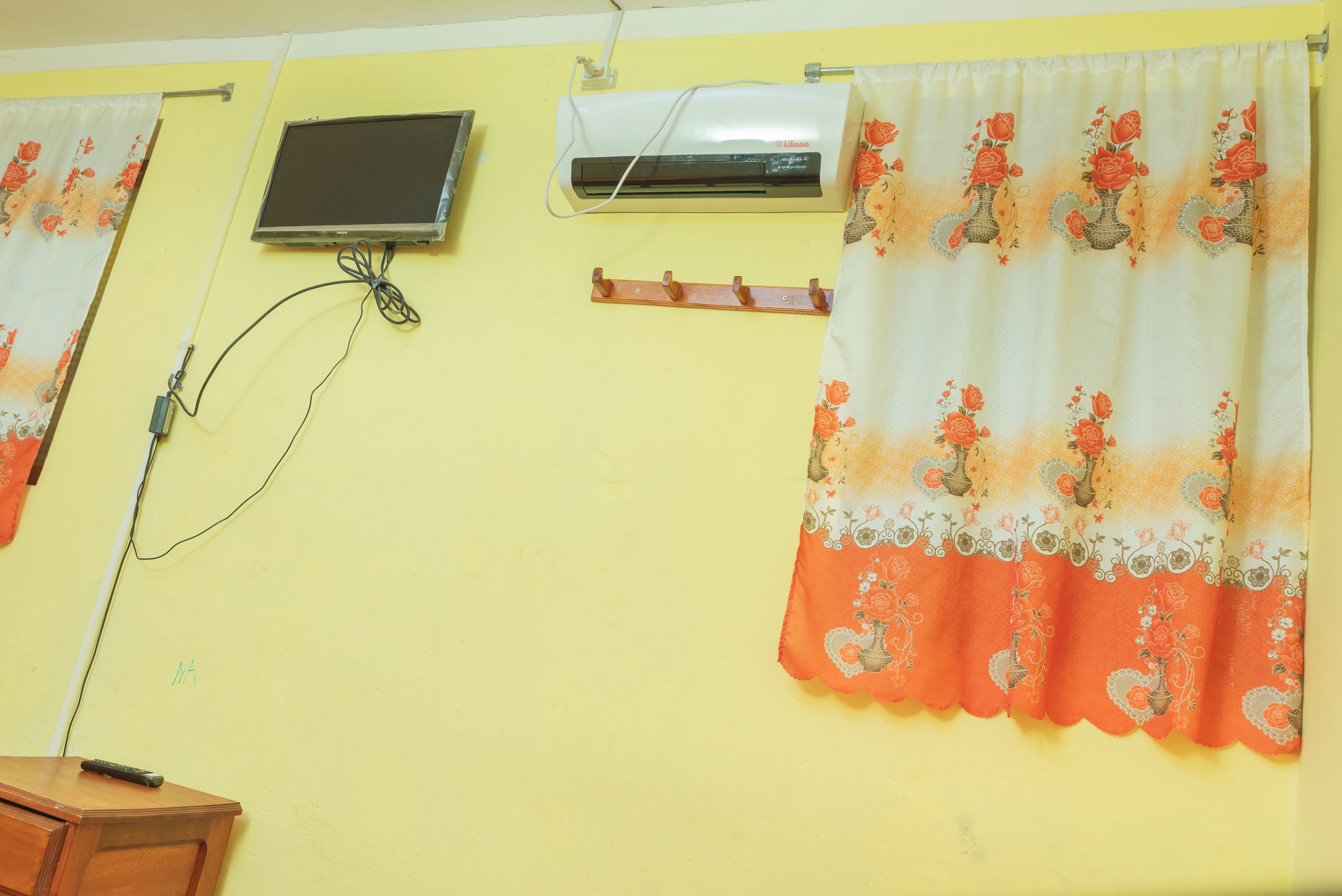 A room with a yellow wall, a flat-screen TV mounted on the wall, an air conditioning unit, and a wooden cabinet.