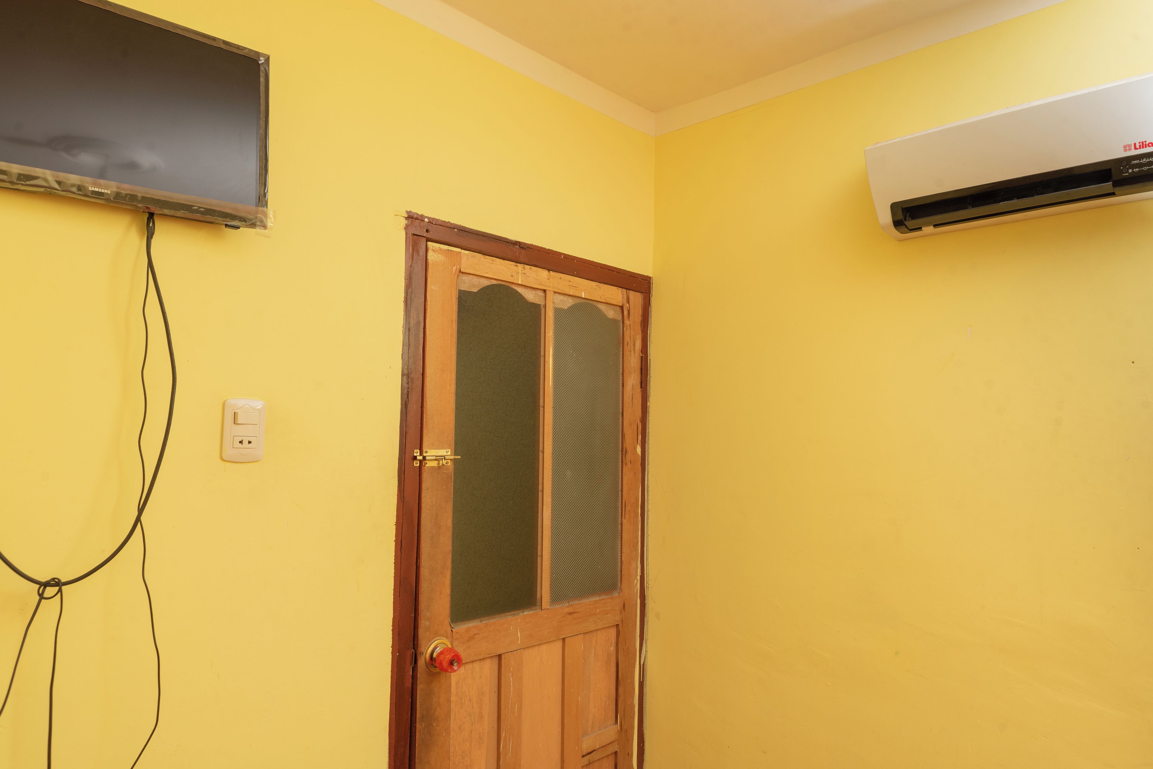 Quarto com porta de madeira, ar-condicionado fixado na parede e televisão na parede.