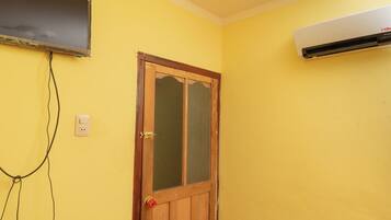 Quarto com porta de madeira, ar-condicionado fixado na parede e televisão na parede.