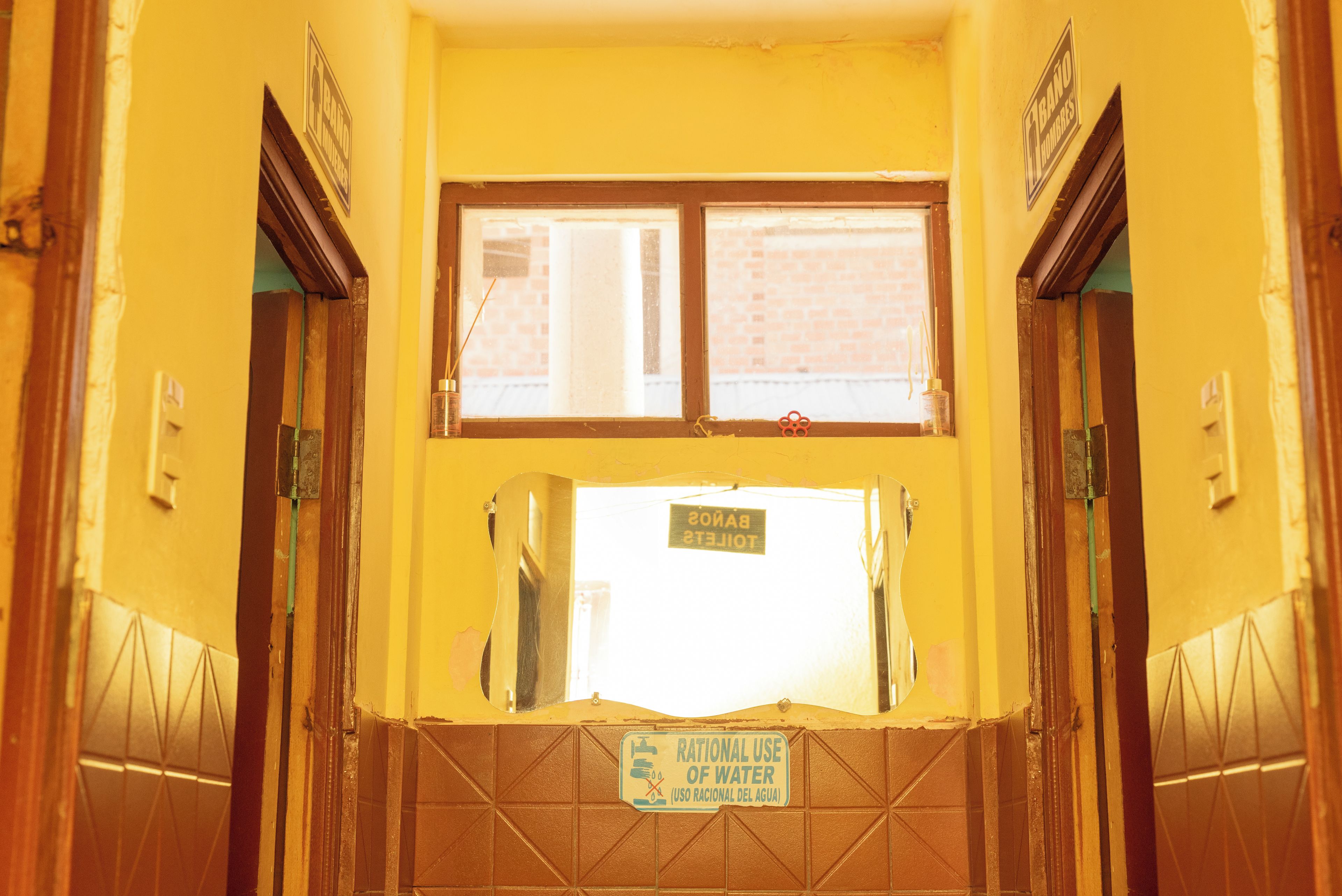 Casa de banho com parede amarela, janela e placa com a mensagem 'Uso Racional da Água'.