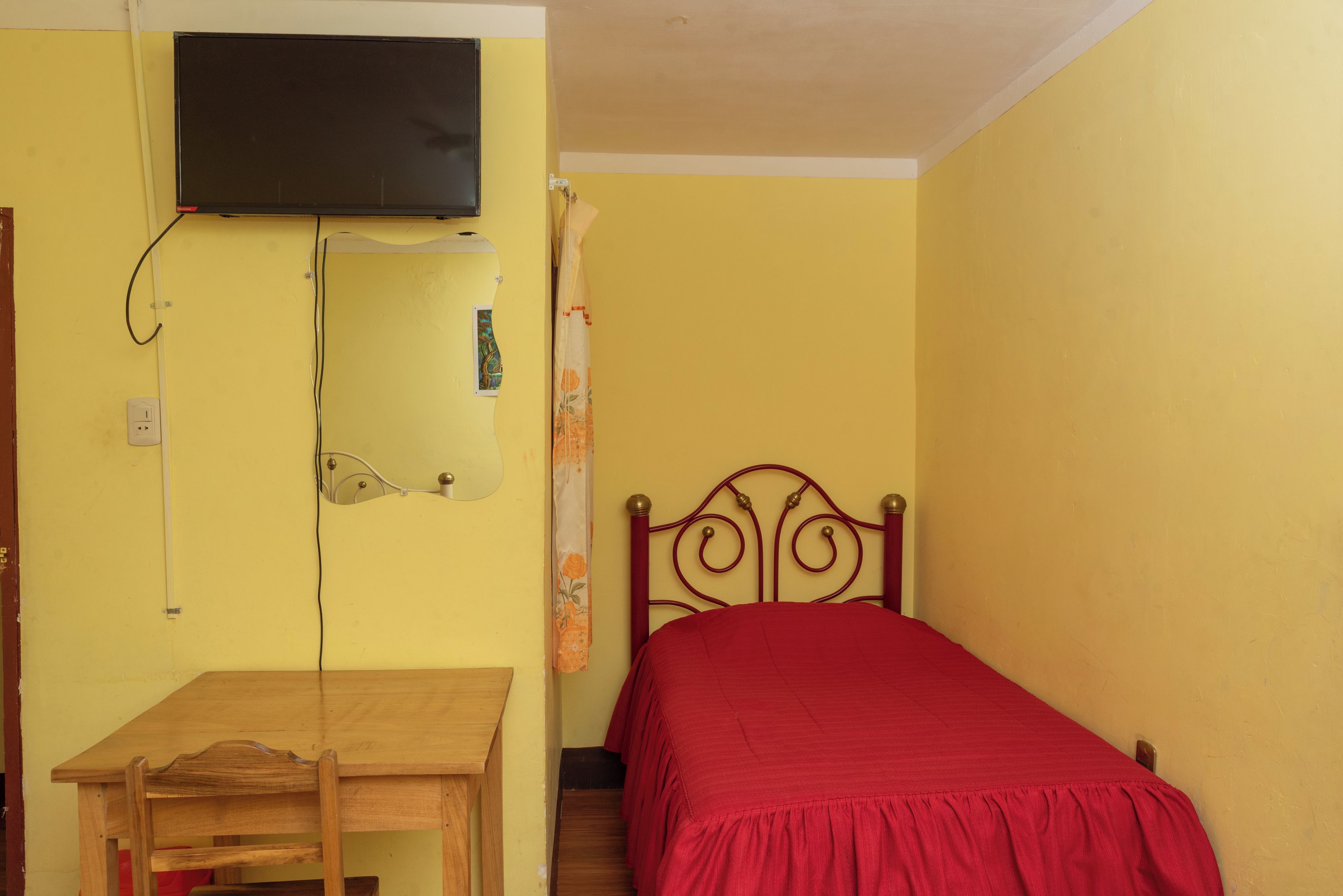 A room with a bed, a desk, and a television mounted on the wall.