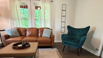 Een woonkamer met een bruine leren bank, een blauwgroene fauteuil en een salontafel.
