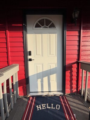 A white door with a 'HELLO' mat in front, set against a red building facade.