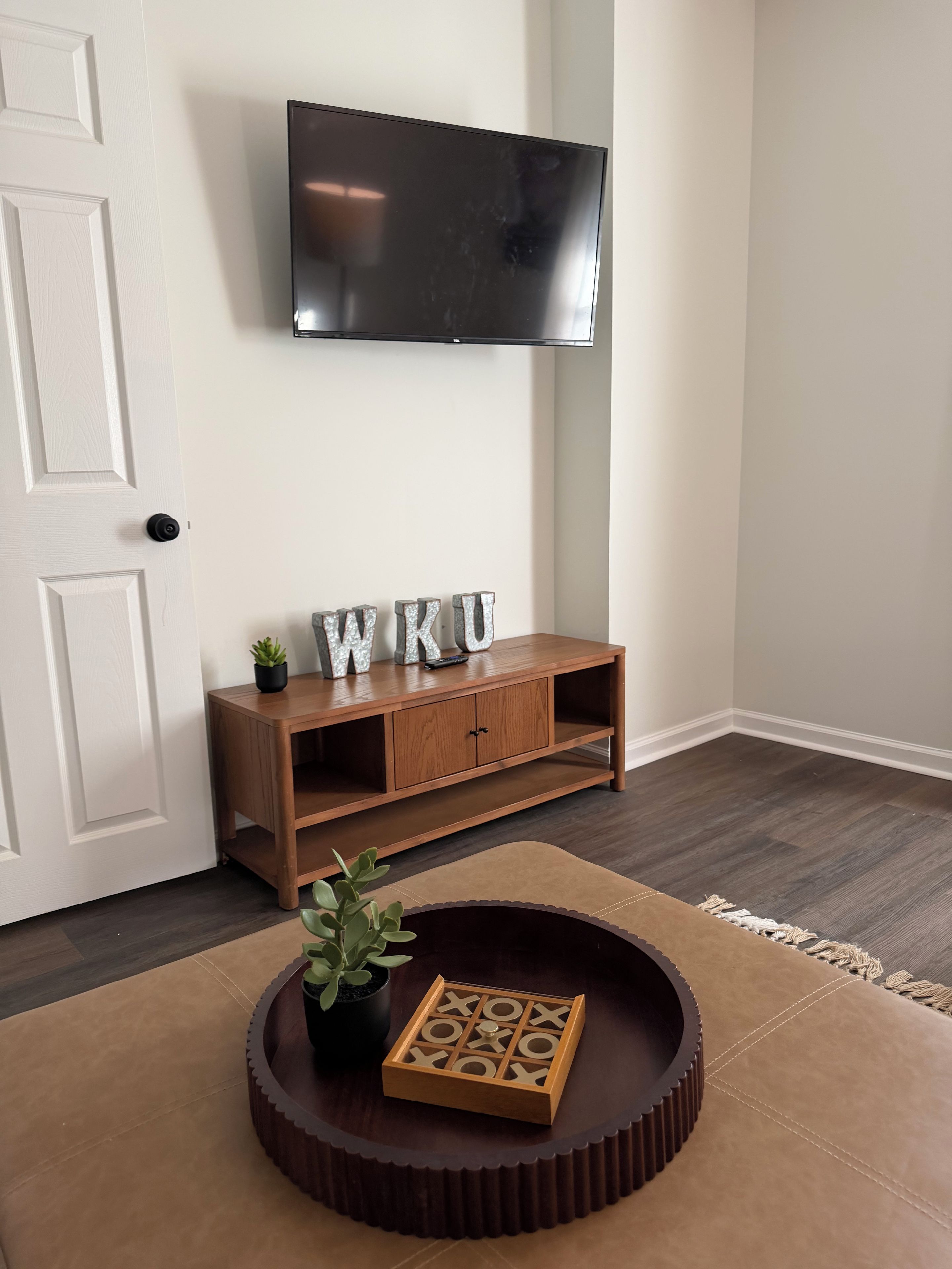 A room with a wooden console table, a television mounted on the wall, and a round coffee table with a wooden tray.
