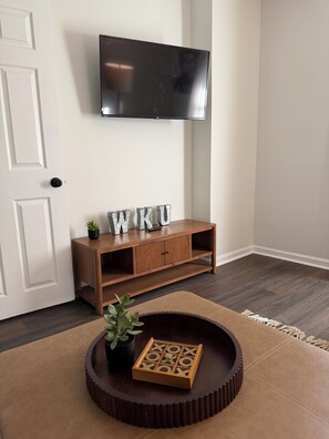A room with a wooden console table, a television mounted on the wall, and a round coffee table with a wooden tray.