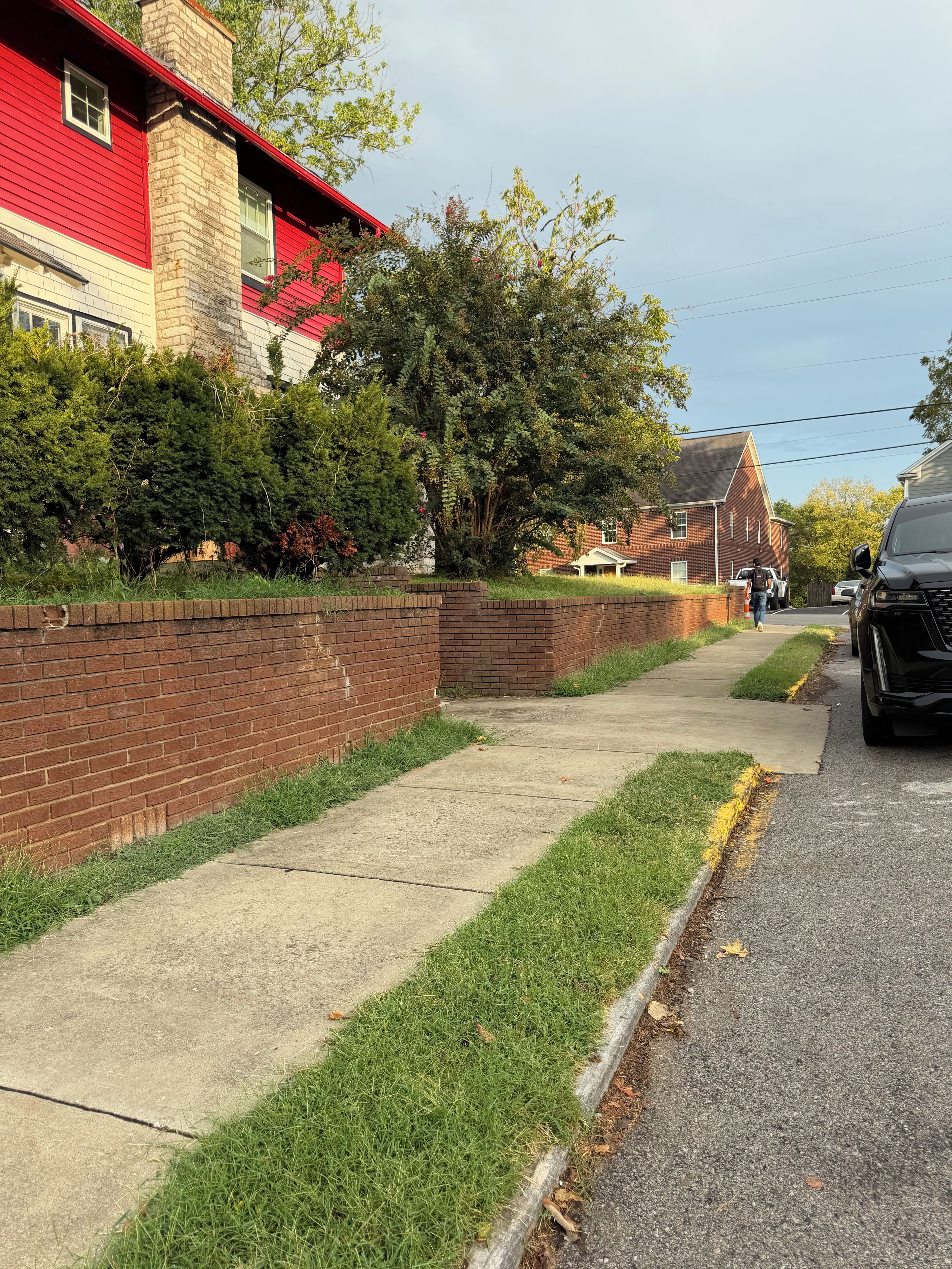 Une rue résidentielle bordée d’un trottoir, d’un mur de briques et d’une maison rouge.