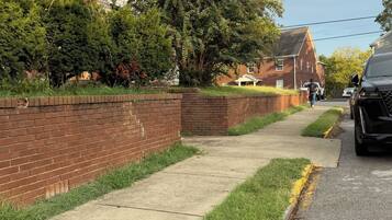 Une rue résidentielle bordée d’un trottoir, d’un mur de briques et d’une maison rouge.