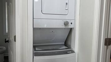 Una lavanderia compatta e bianca con lavatrice e asciugatrice integrate, un pannello di controllo e un piccolo ripiano.