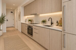 Una cocina moderna con armarios de madera clara, electrodomésticos de acero inoxidable y horno empotrado.