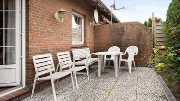 Eine Terrasse mit weißen Plastikstühlen und einem Tisch, einer Ziegelwand und einer Satellitenschüssel.