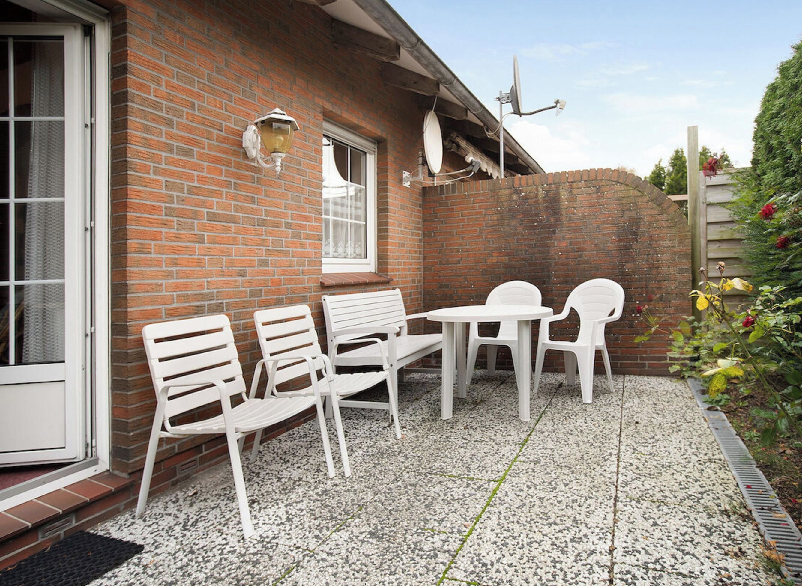 Une terrasse avec des chaises et une table en plastique blanc, un mur de briques et une fenêtre.