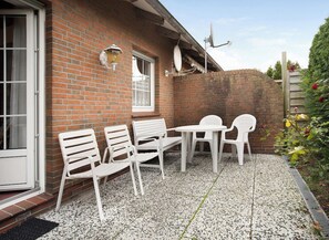 Un patio con sillas y una mesa de plástico blanco, un muro de ladrillo y una ventana.