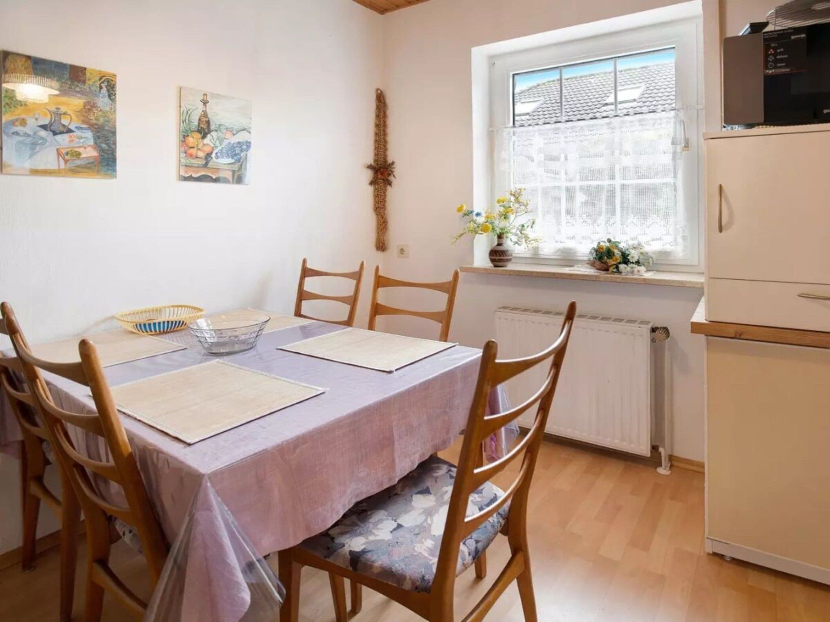A dining area with a table set for four, wooden chairs, a window with a view, and a radiator.