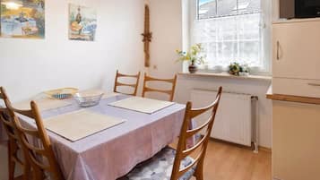 A dining area with a table set for four, wooden chairs, a window with a view, and a radiator.