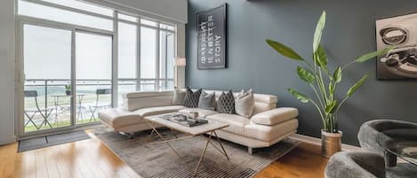 A modern living room with a large window, a white sofa, a coffee table, and a potted plant.