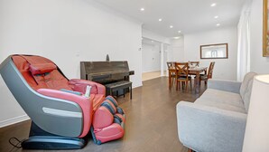 Uma sala de estar moderna com uma poltrona de massagem, um piano, uma mesa de jantar com cadeiras e um sofá.