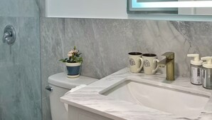 Casa de banho com cabine de duche em vidro, lavatório de mármore e sanita branca.