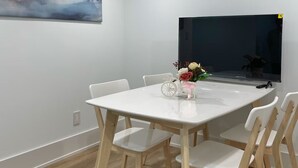 Uma sala de jantar moderna com uma mesa e cadeiras brancas, uma televisão de tela plana e um quadro na parede.