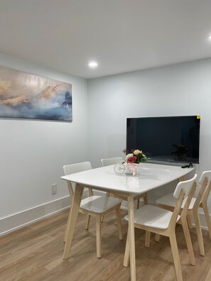 Et moderne spiseområde med et hvidt bord og stole, et fladskærms-tv og et billede på væggen.