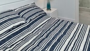 Quarto de hotel com uma cama, mesa de cabeceira, luminária, pintura e banheiro visível por uma porta aberta.